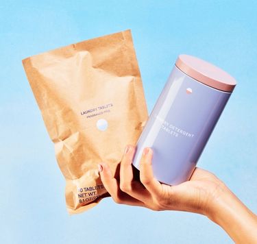 Blueland Laundry refillable tin and tablets in compostable pouch in hand against blue backdrop