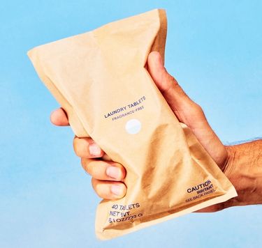Blueland Laundry tablets in compostable pouch in hand against blue backdrop