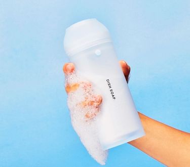 Blueland Powder Dish Soap in refillable silicone shaker in hand against blue backdrop with foam