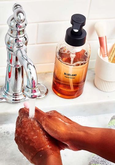 Natural Collection amber hand soap bottle by faucet with water with two hands washing underneath
