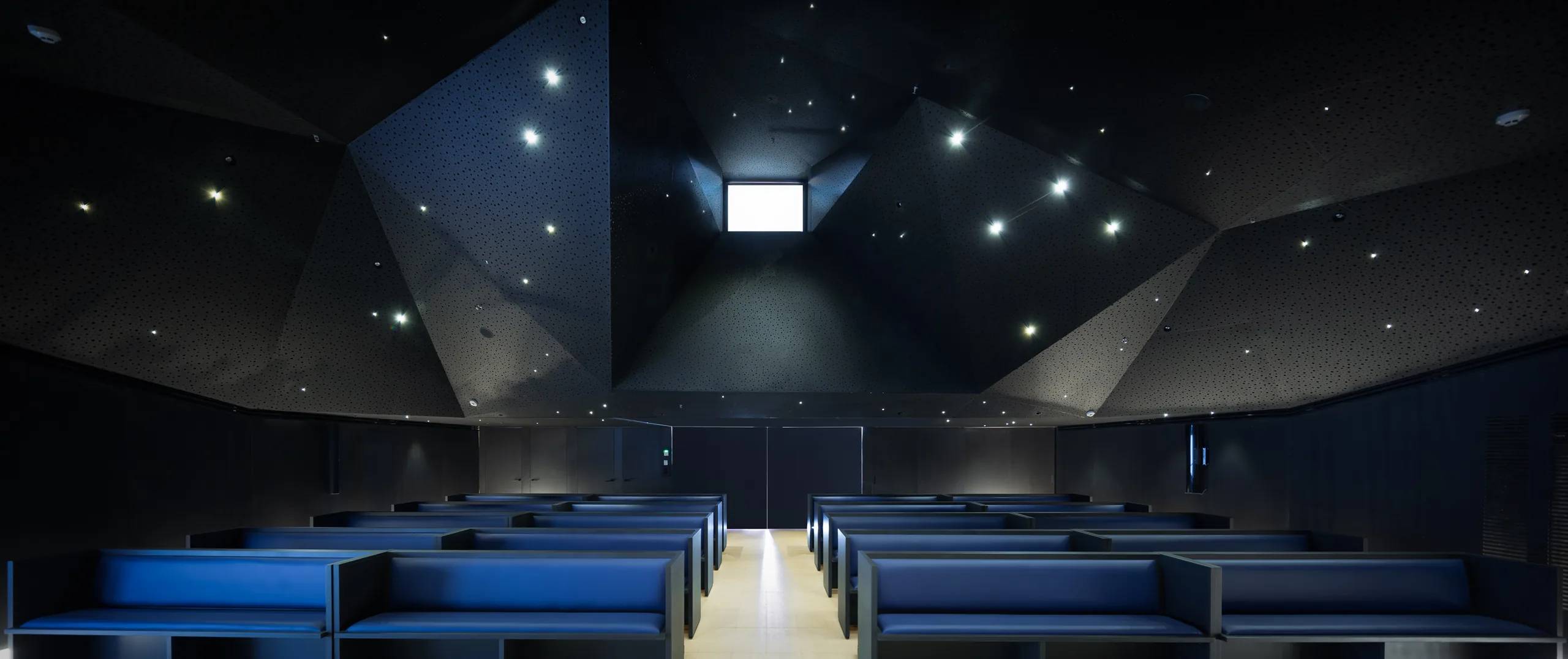 Sala de actos con techo facetado y luminarias puntuales