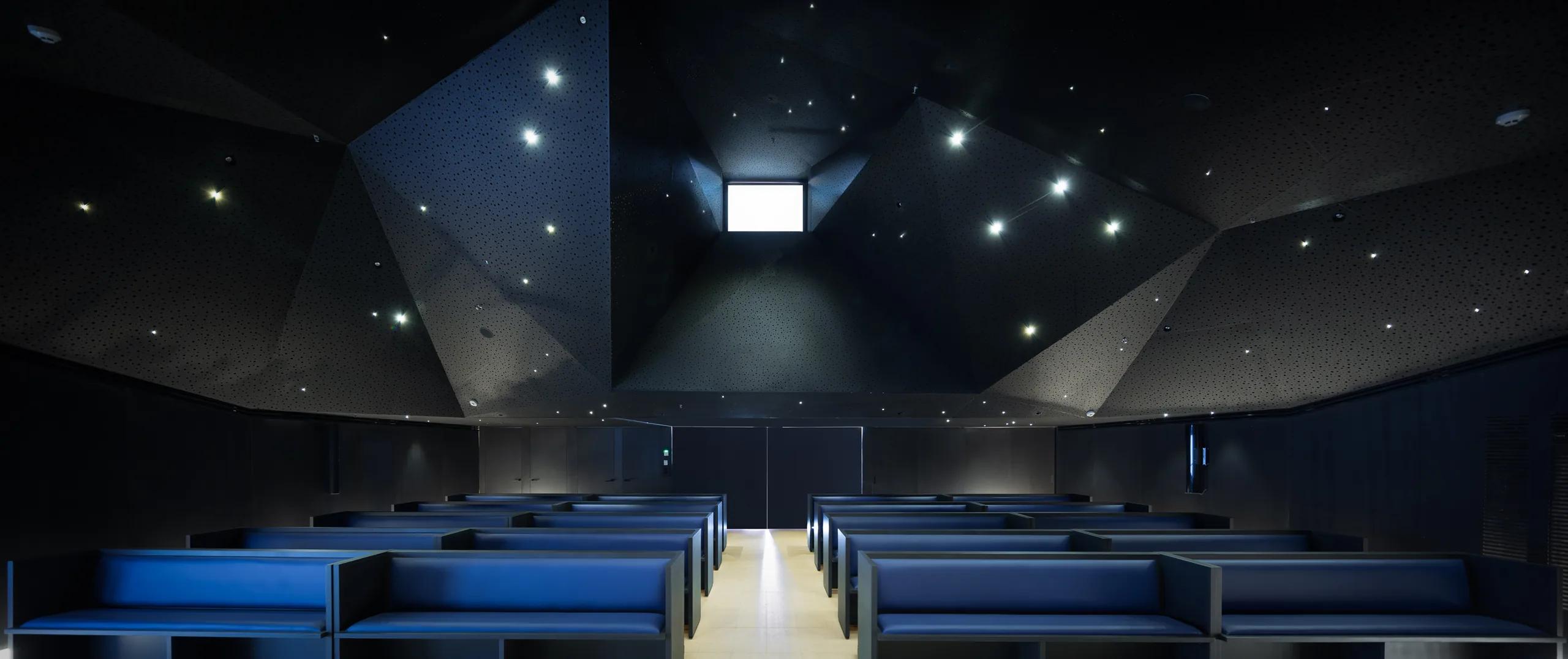 Sala de actos con techo facetado y luminarias puntuales