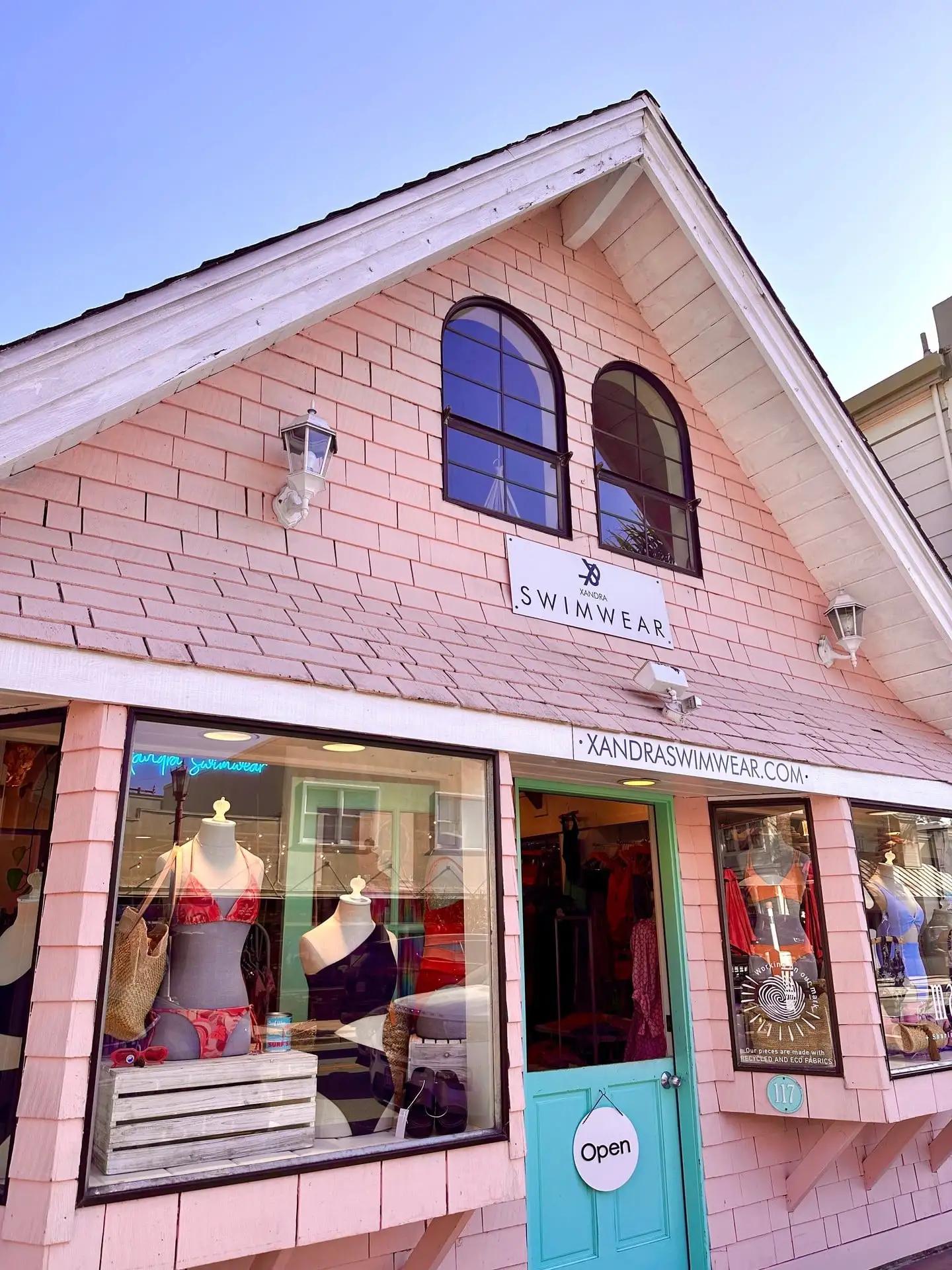 Pink storefront of a boutique with mannequins dressed in swimwear displayed in the window.