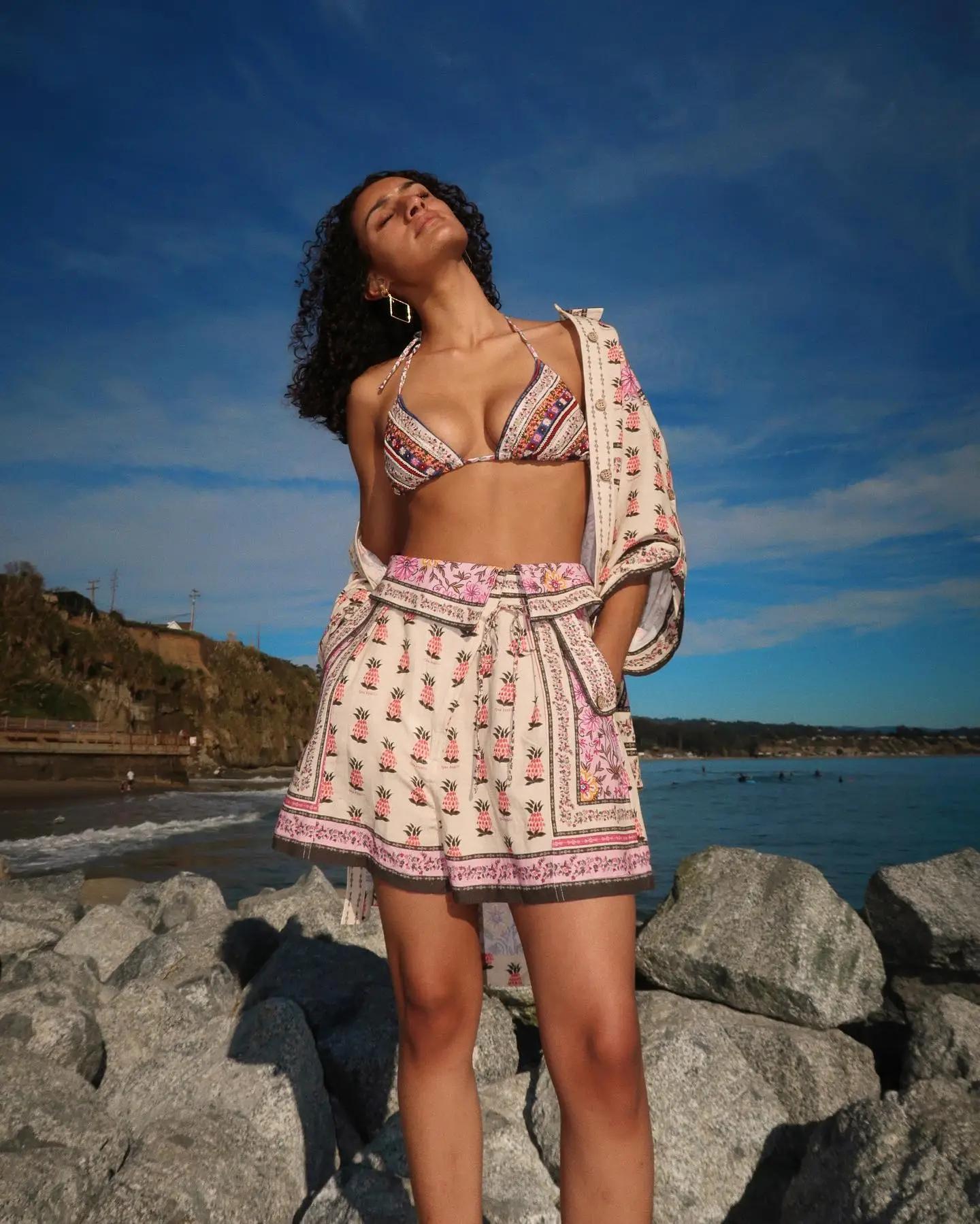 Person standing on rocks by the sea, wearing a light-colored summer dress.