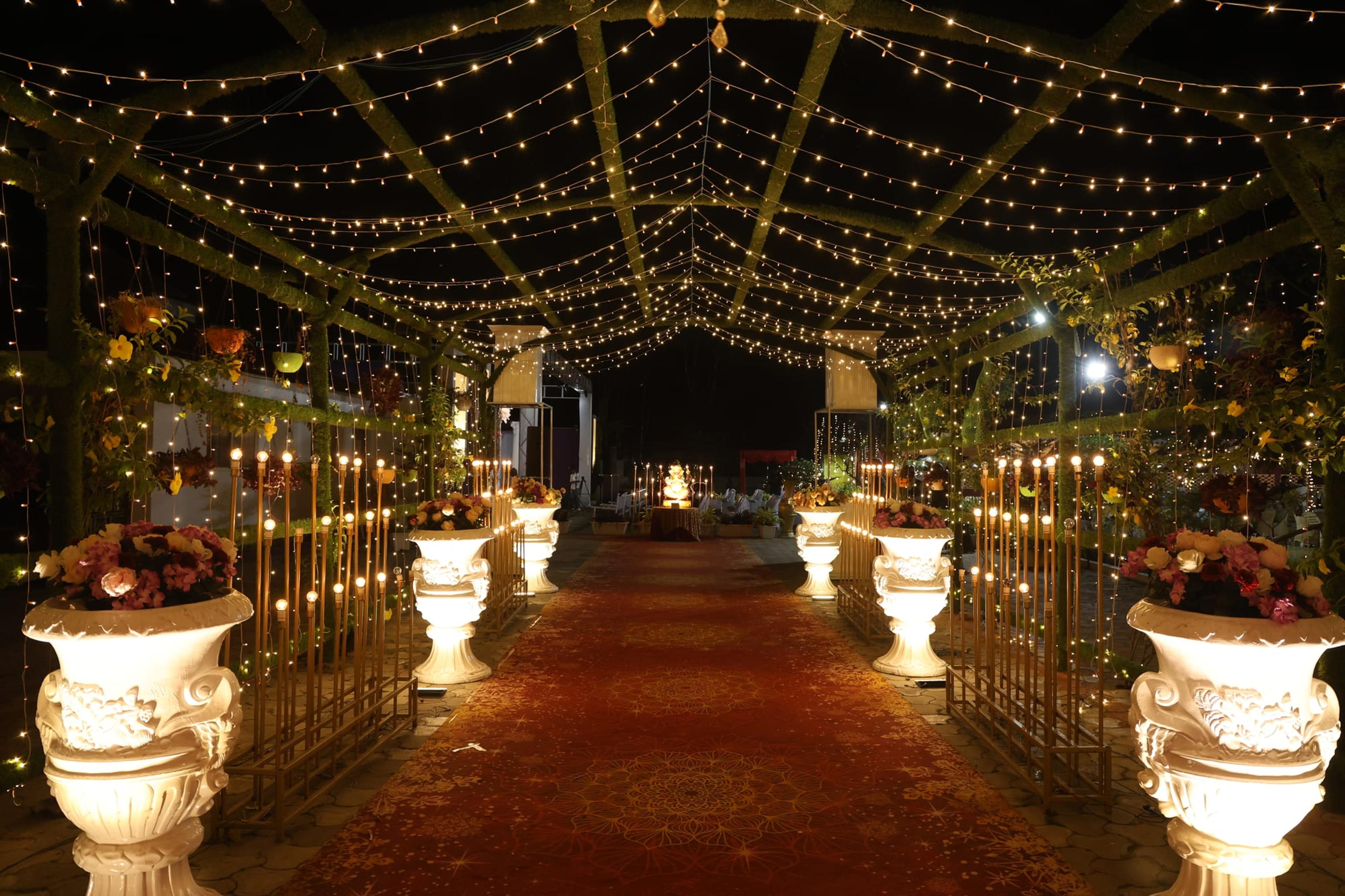 A fairy-light canopy entrance walkway lined with illuminated floral urns leading to a glowing stage