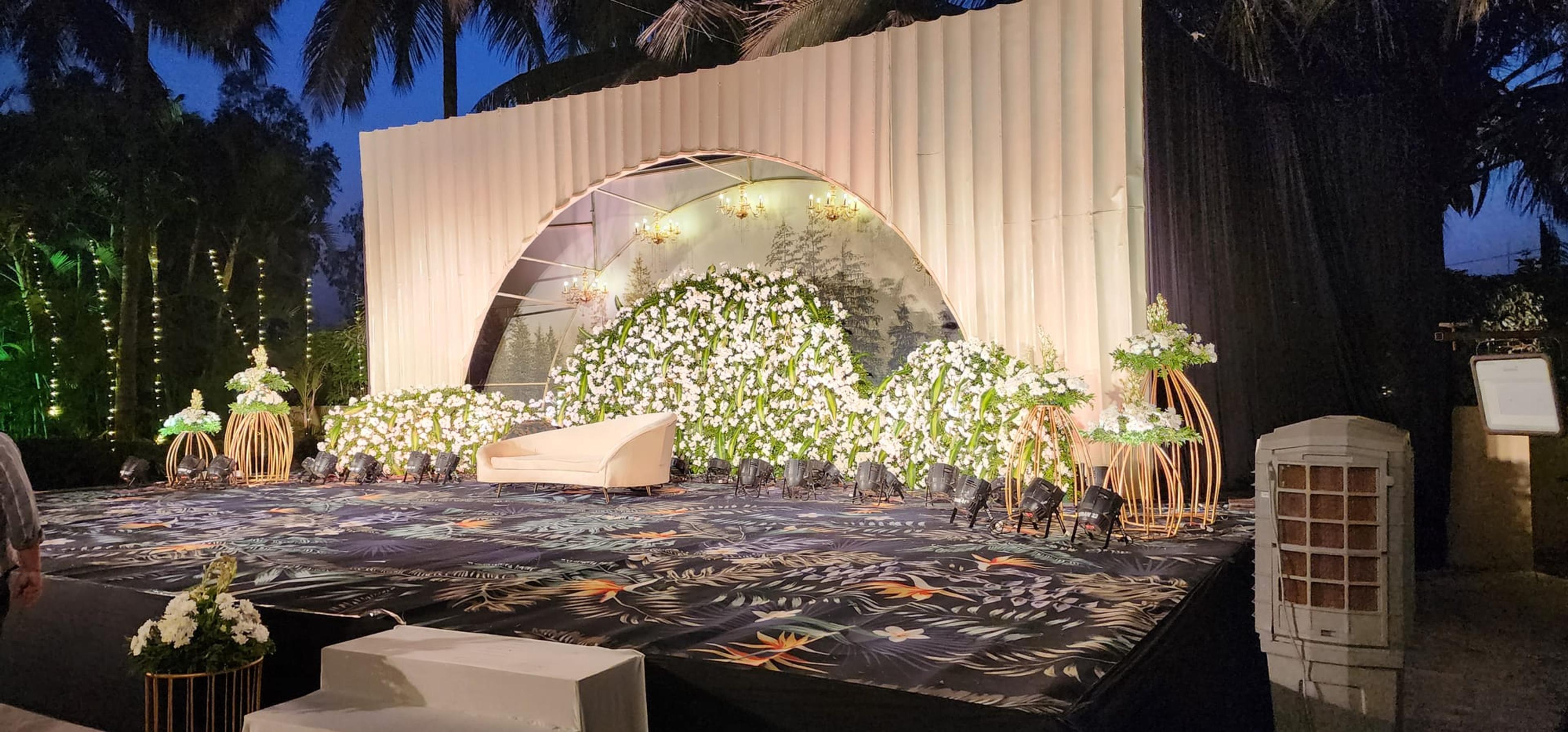 A glowing white-and-gold floral reception stage with a domed backdrop framed by tall gold candle stands