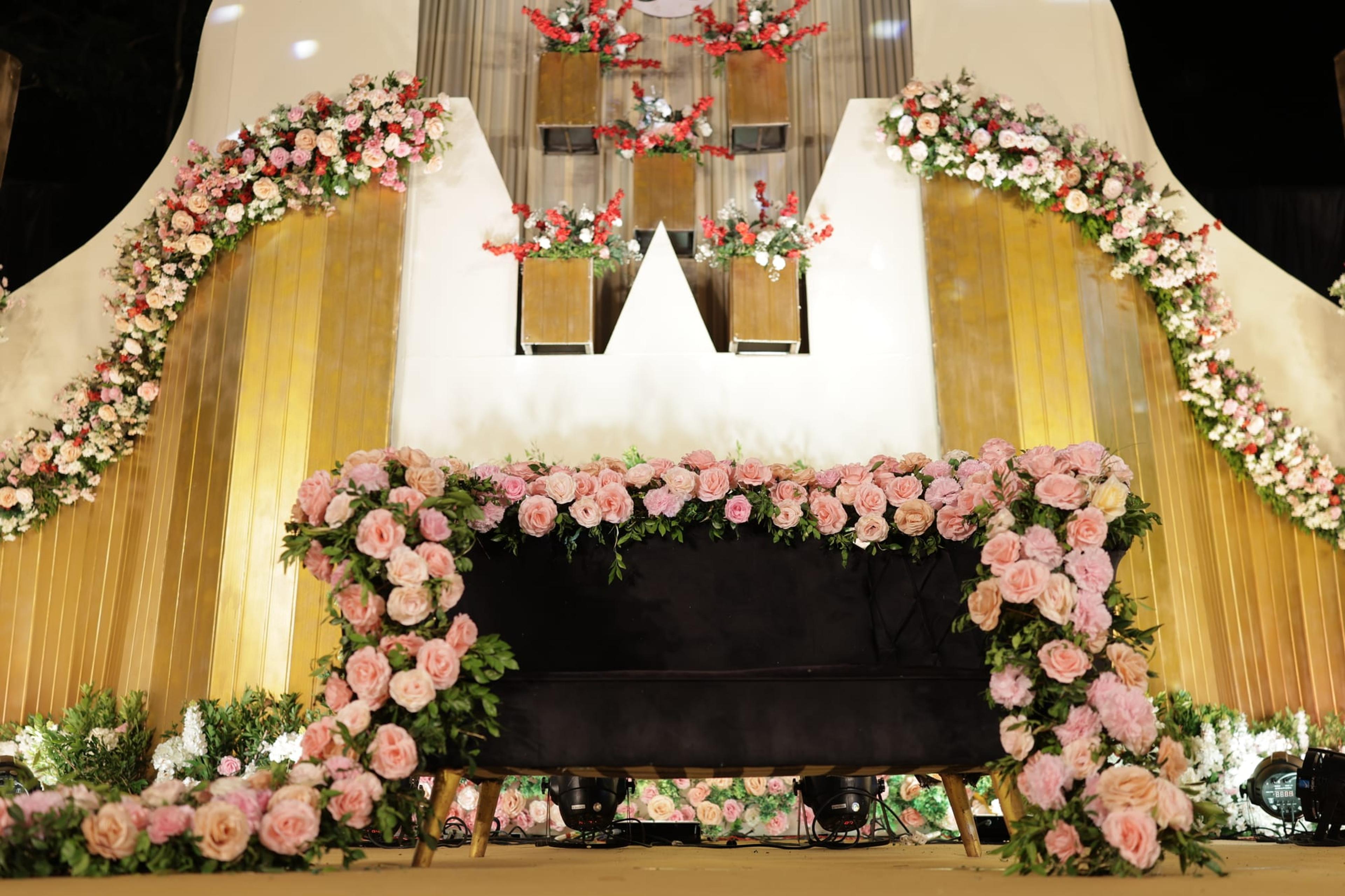 Grand gold-draped reception stage banked with peach floral garlands and crimson roses under warm lighting