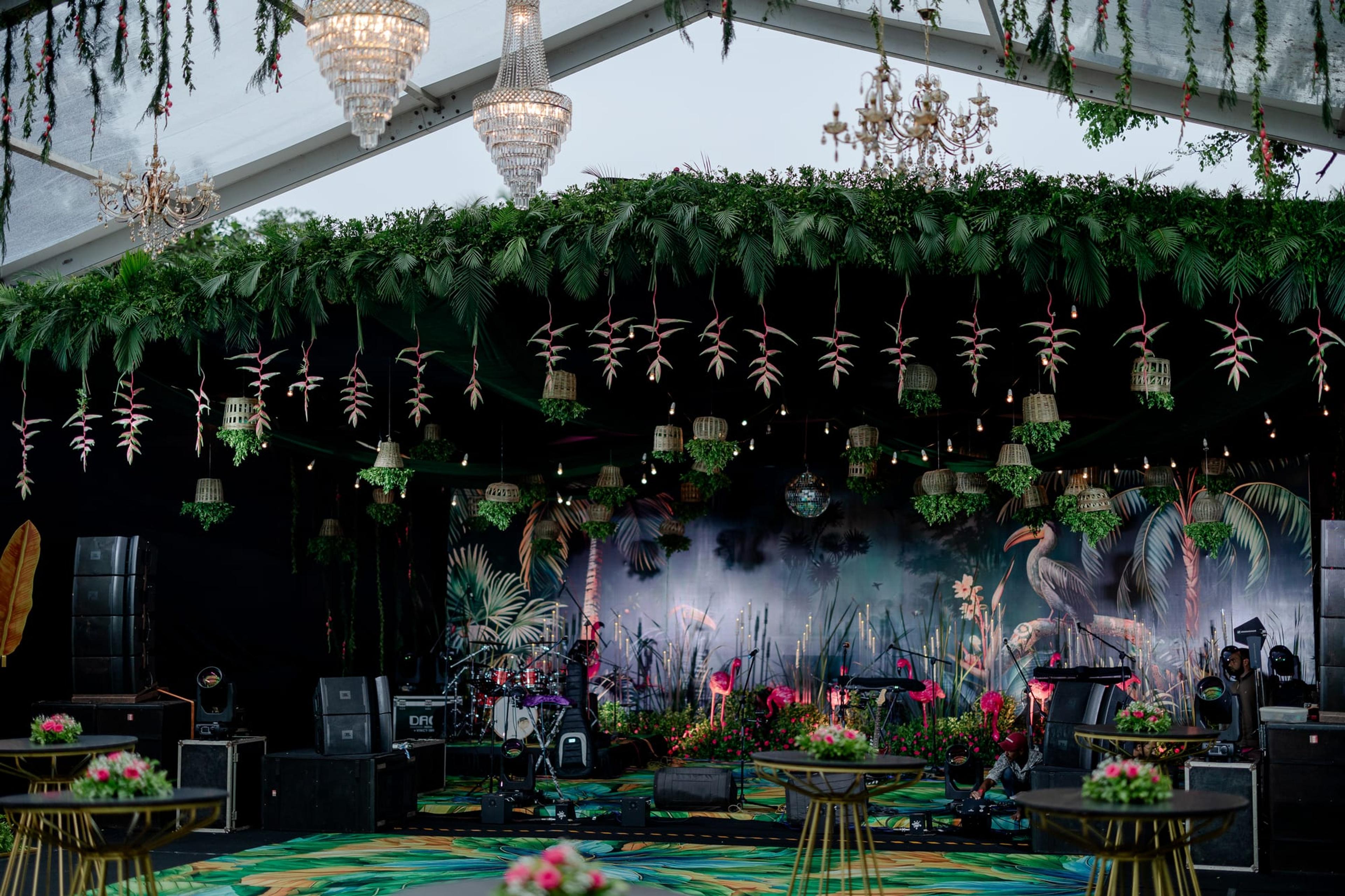 Tropical glasshouse stage under a thick canopy of hanging greenery and crystal chandeliers, with pink flamingo sculptures