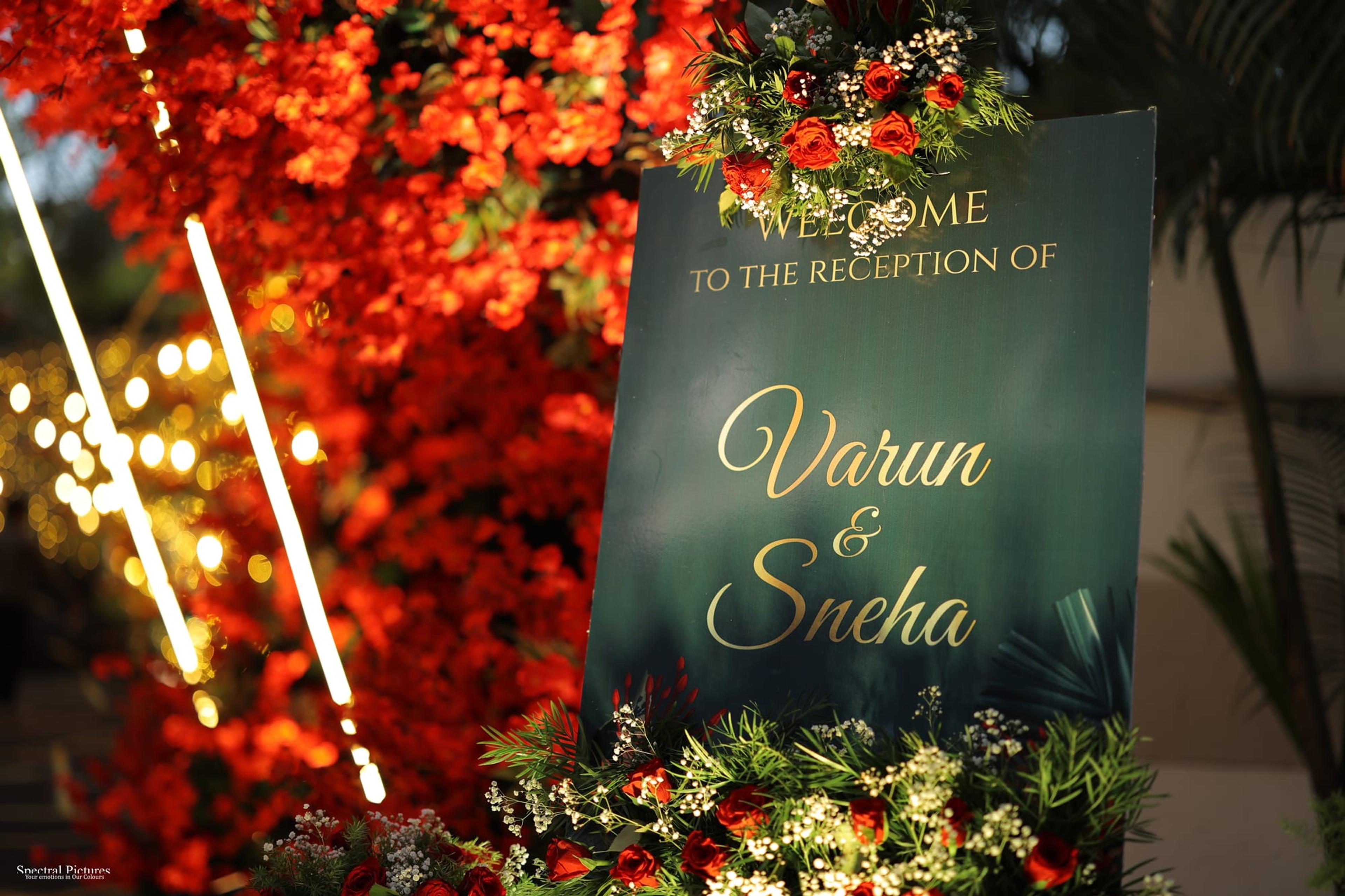 An illuminated welcome sign set within a dense canopy of red blossoms and warm fairy lights at night