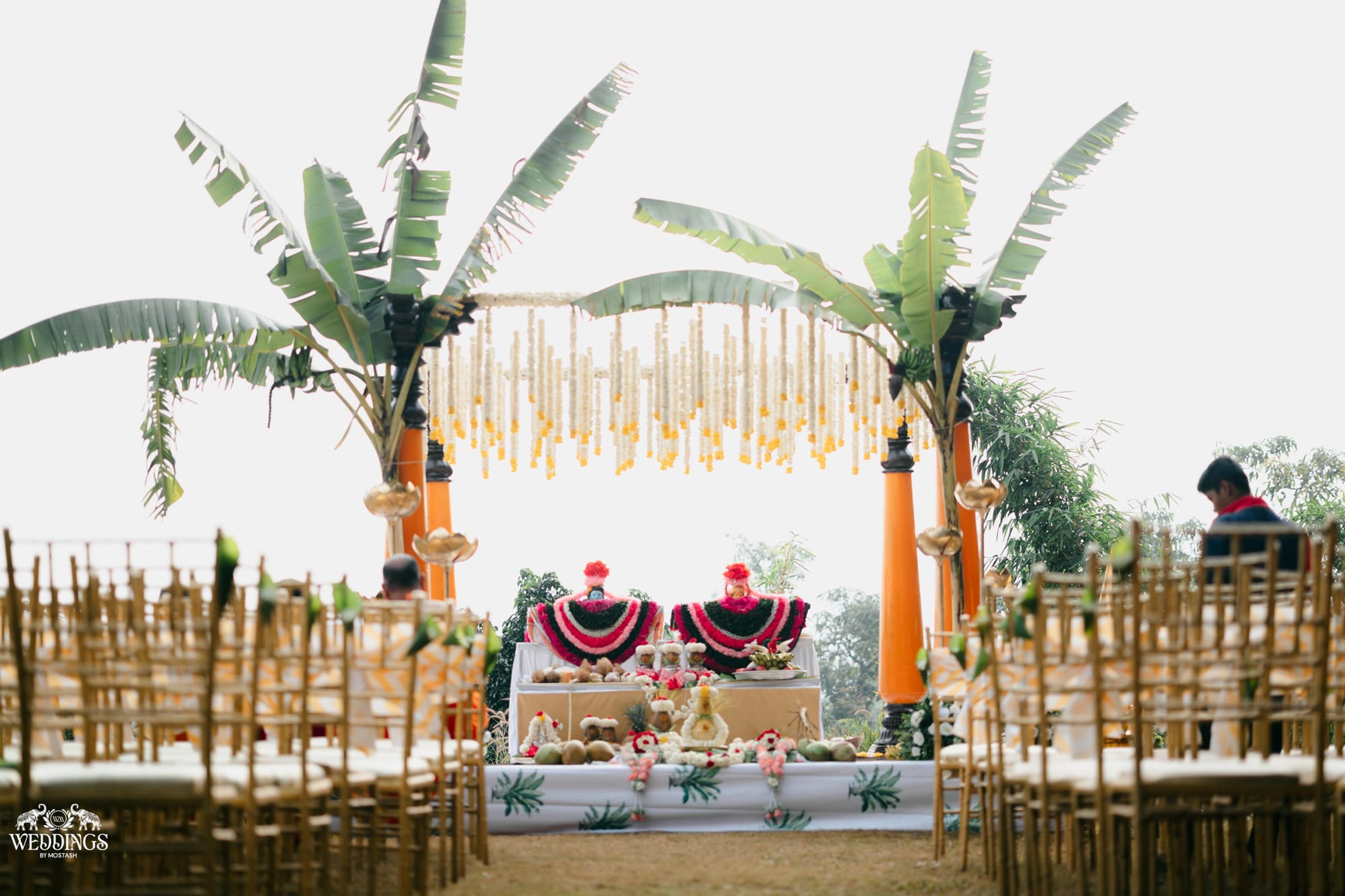 A banana-leaf and marigold ceremony mandap on an open lawn with bamboo seating