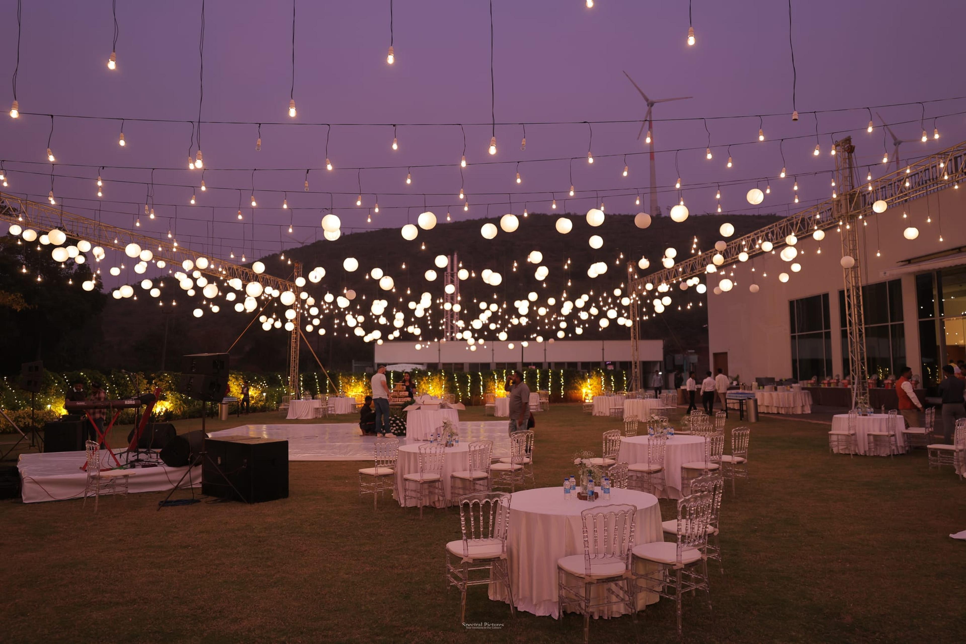 An open-air reception glowing under a vast canopy of warm string lights against a deep purple dusk sky