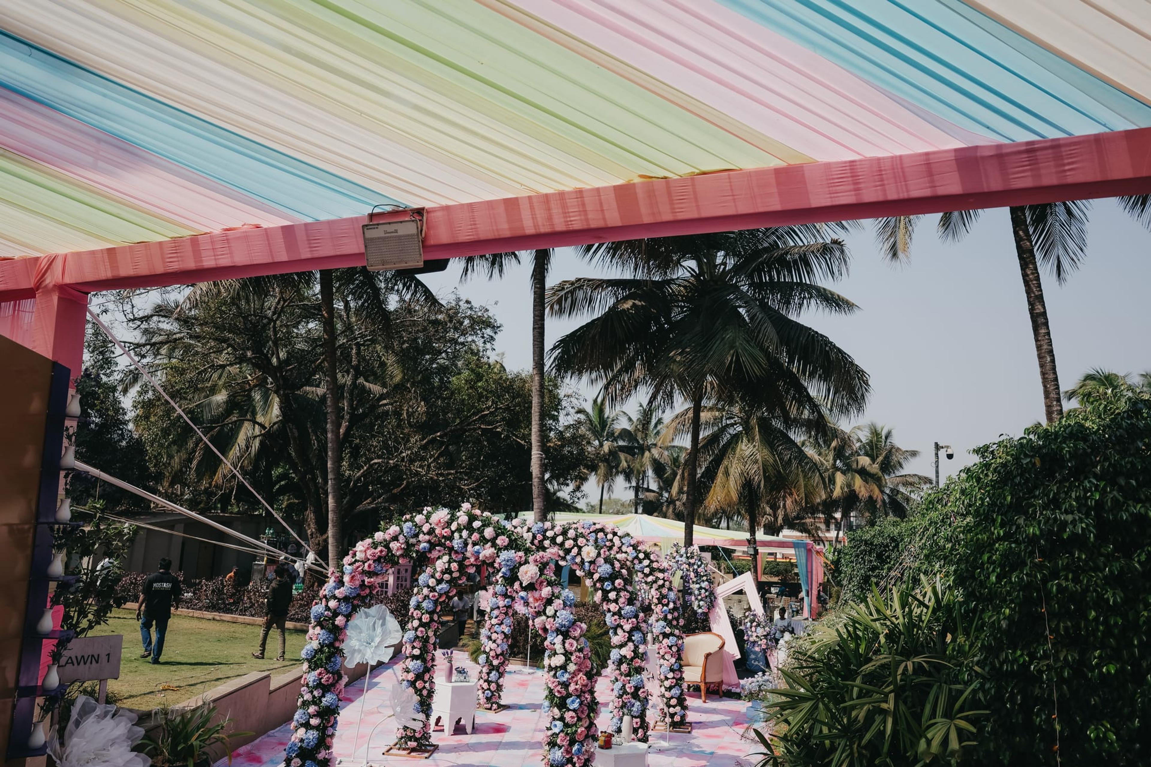 Rainbow-draped garden walkway lined with a multicolour floral aisle leading to a pastel ceremony stage