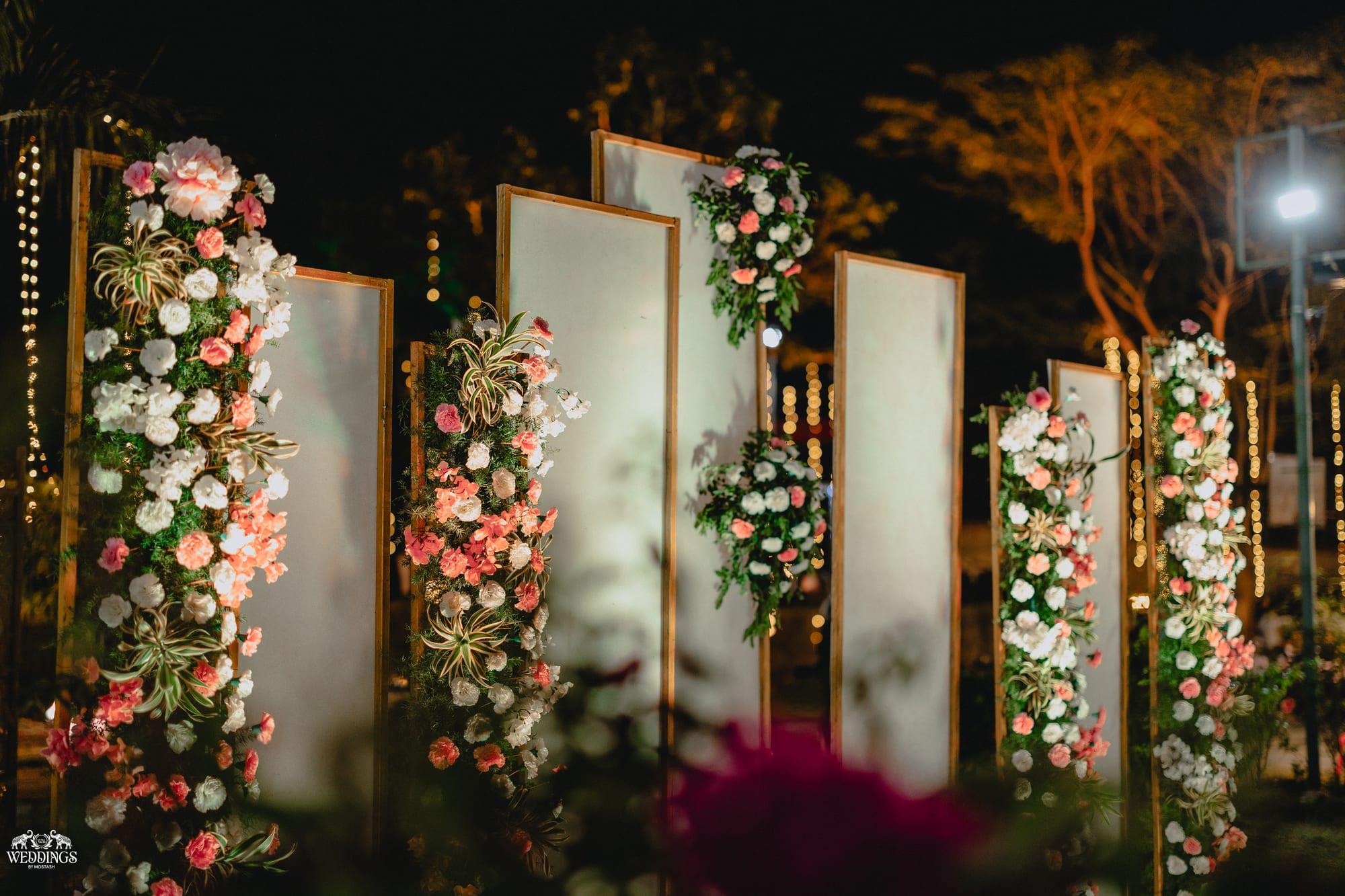 Tall garden pillars wrapped in fuchsia and white blooms glowing under fairy lights at an ivory-and-green evening wedding