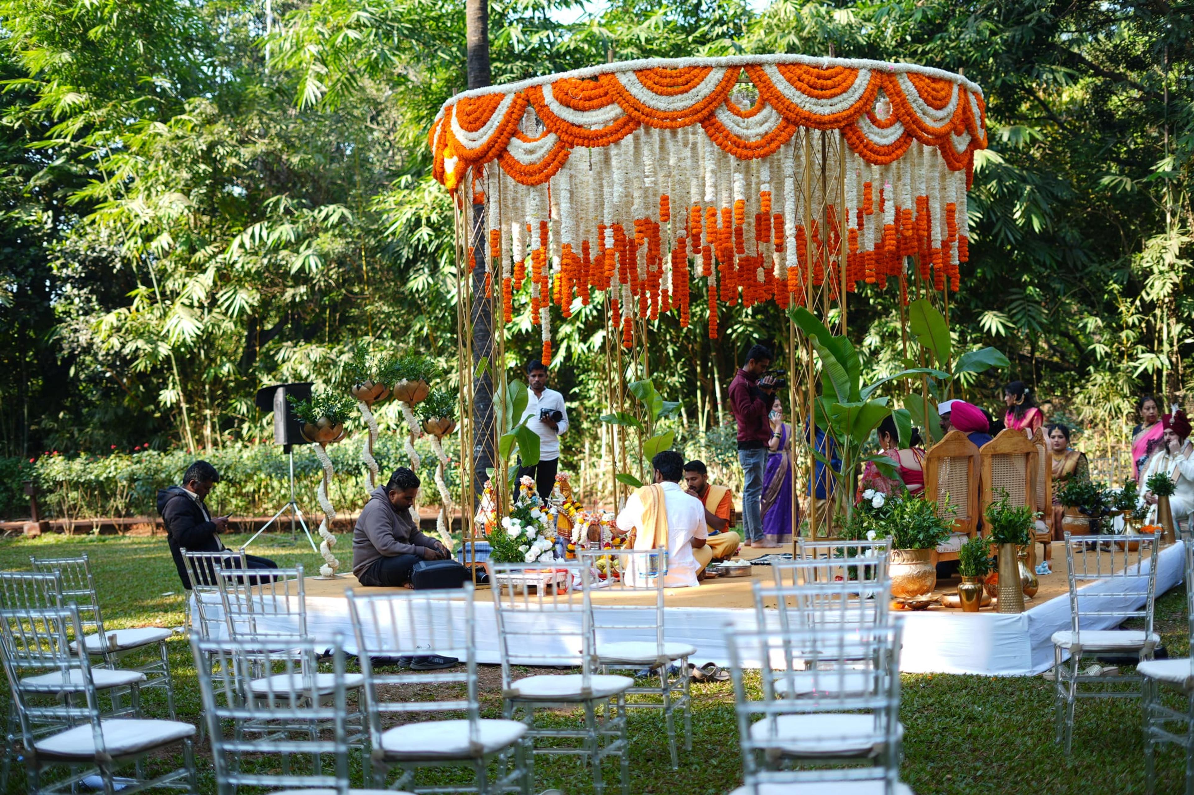 A vibrant marigold-draped canopy mandap set on a tropical garden lawn lined with chiavari chairs and palms