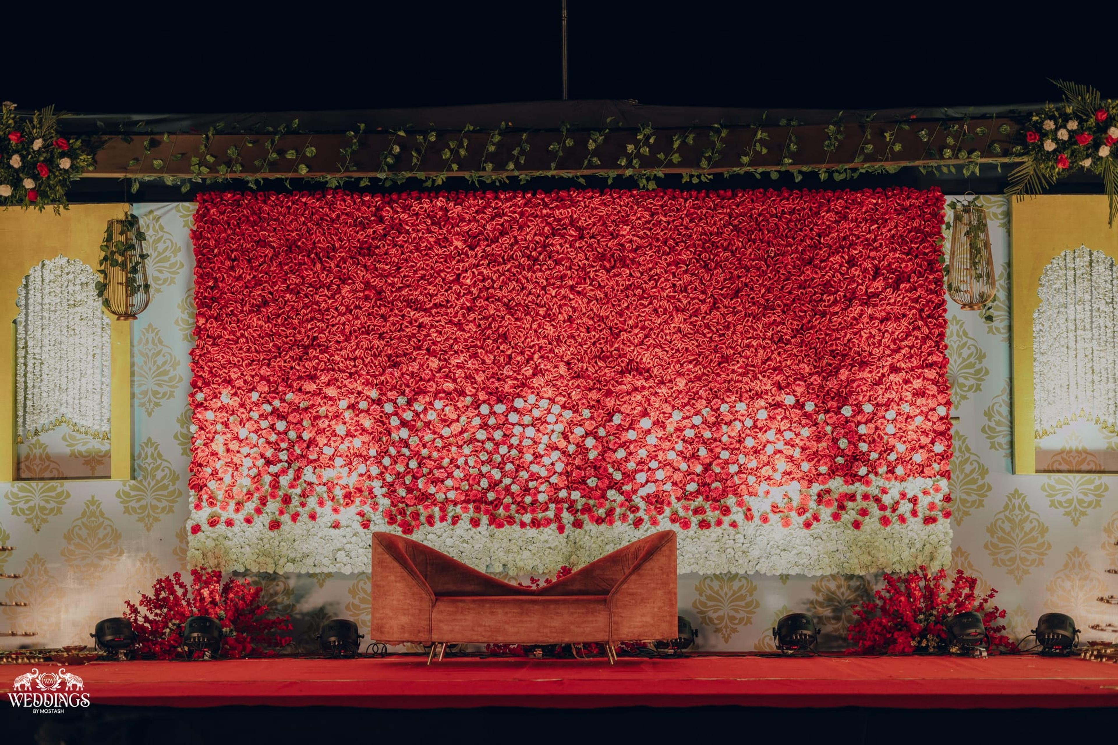 A lush red rose-petal stage backdrop with a gilt-accented seat glowing under warm light