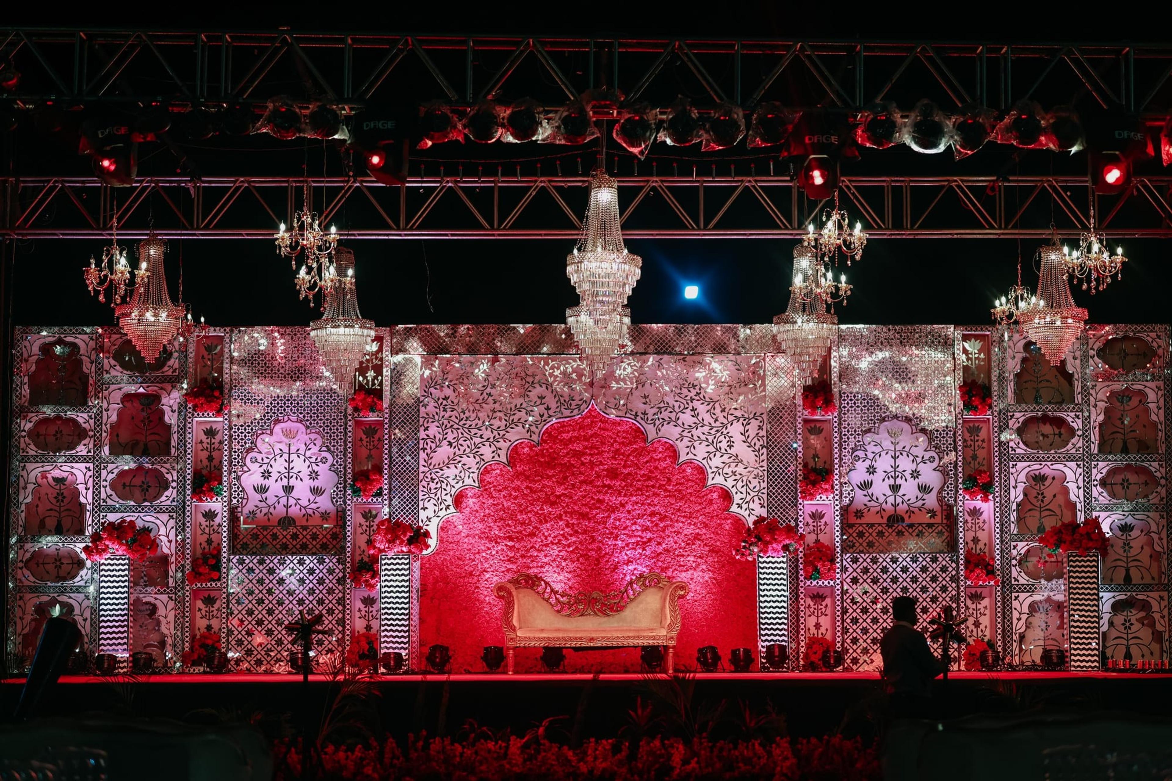 Grand red-and-gold reception stage with crystal chandeliers and a carved floral mandala throne