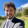 a man in a suit and tie smiles in front of a mountain