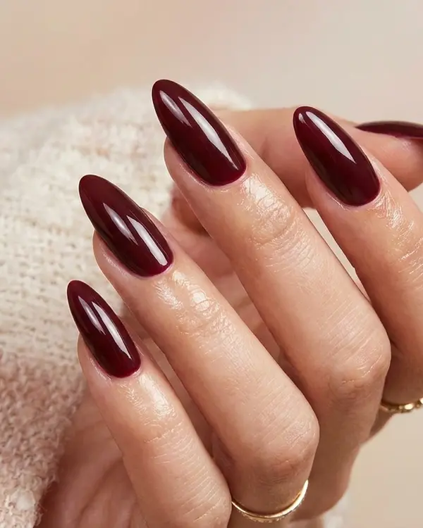 Hand with long almond-shaped acrylic nails in a deep maroon colour with high-gloss finish.