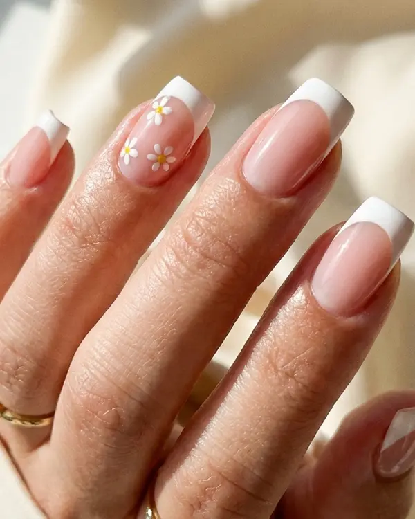 Hand with classic French tip manicure and tiny hand-painted white flowers on accent nails.