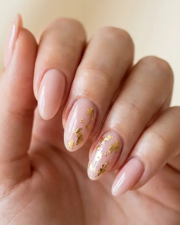Close-up of a hand with glossy gel manicure nails accented by delicate gold foil details.