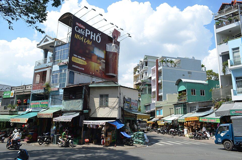 Local shops, awnings and motorbikes on a sunny street corner in Chợ Lớn