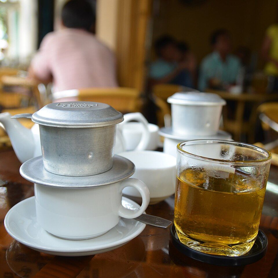Vietnamese phin coffee filters, cups and tea on a table at a sidewalk café in Saigon