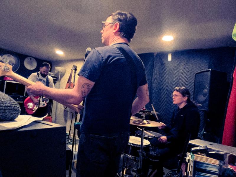A dark photo of the musicians in the band bobcat, in a basement room, practicing a song.