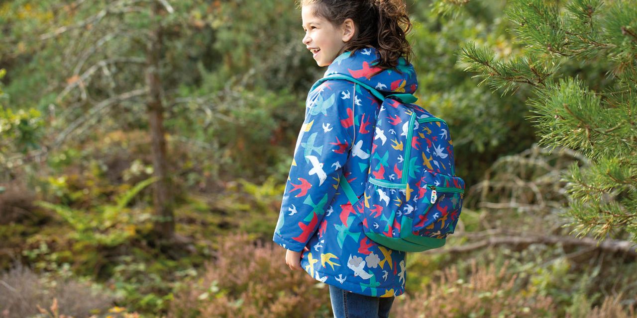 Tjej som står i skogen klädd i en blå jacka med färgglada fåglar och matchande ryggsäck