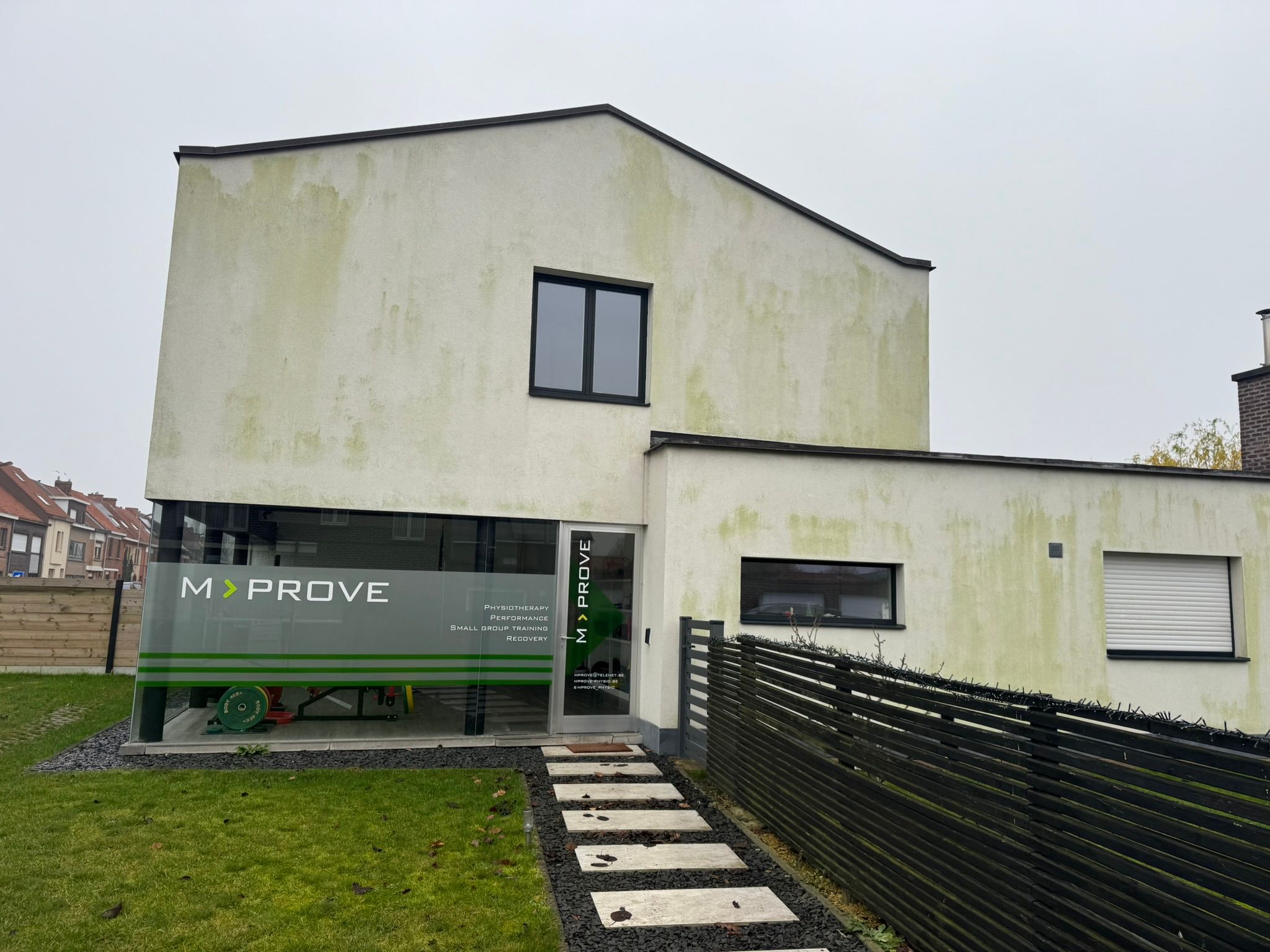 Witte crepi-gevel in Drongen met groene aanslag en algengroei op de gevel