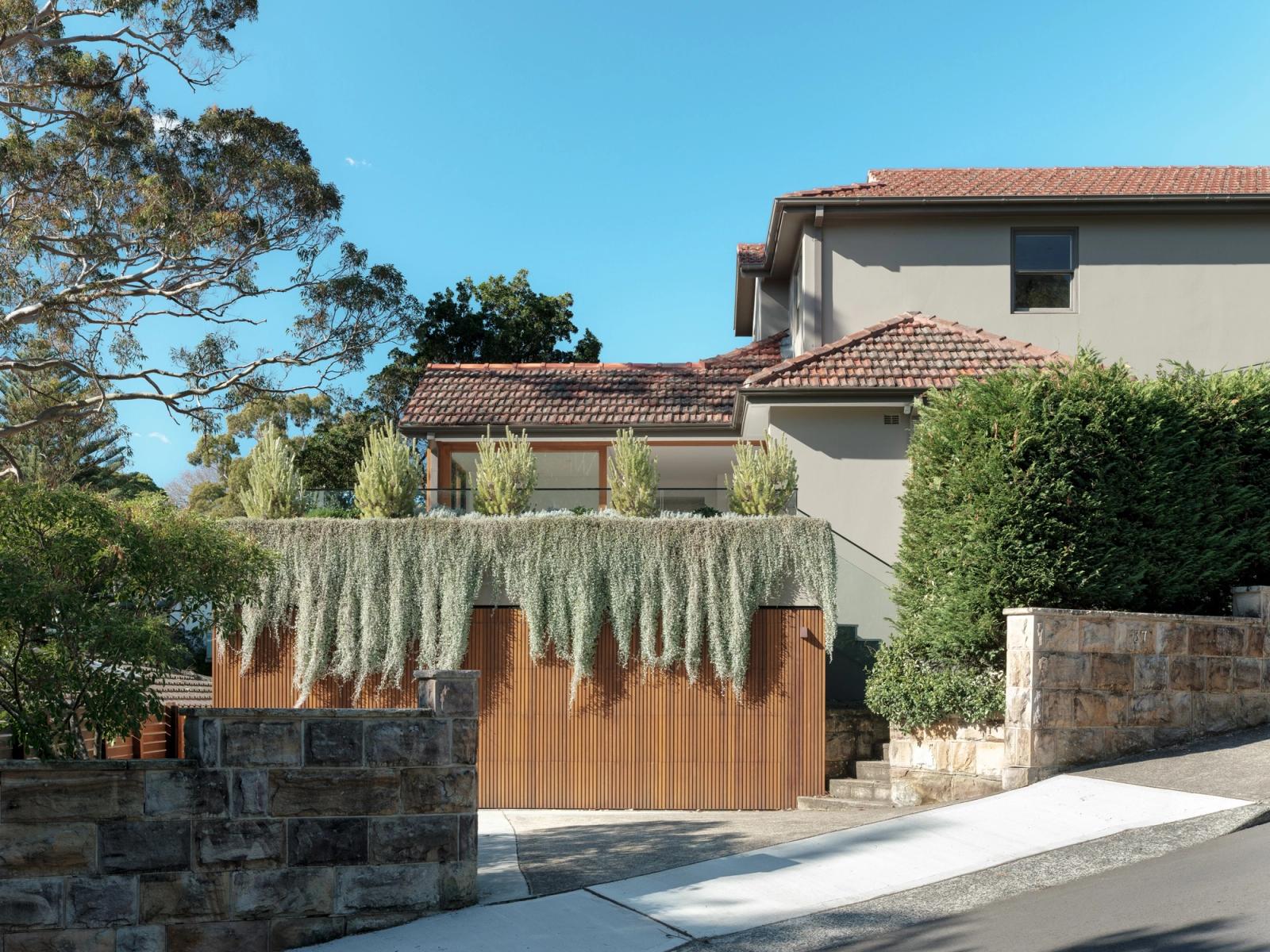 The street elevation: cedar-battened garage door under draping greenery