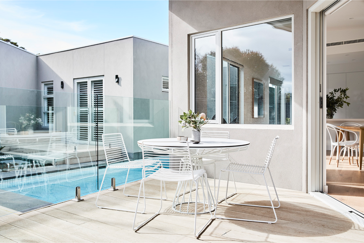 An exterior outdoor patio with a pool, featuring a white table and chairs.