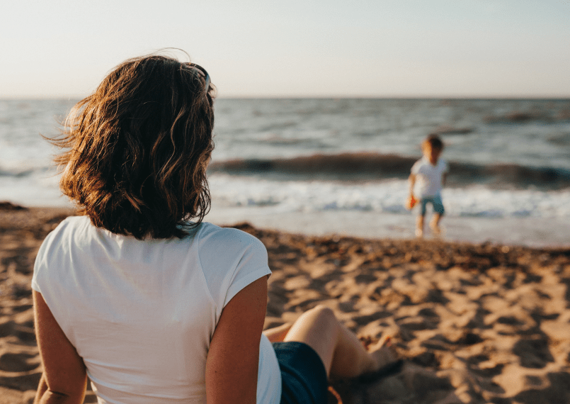 a woman sitting on the beach watching her child playing in the water