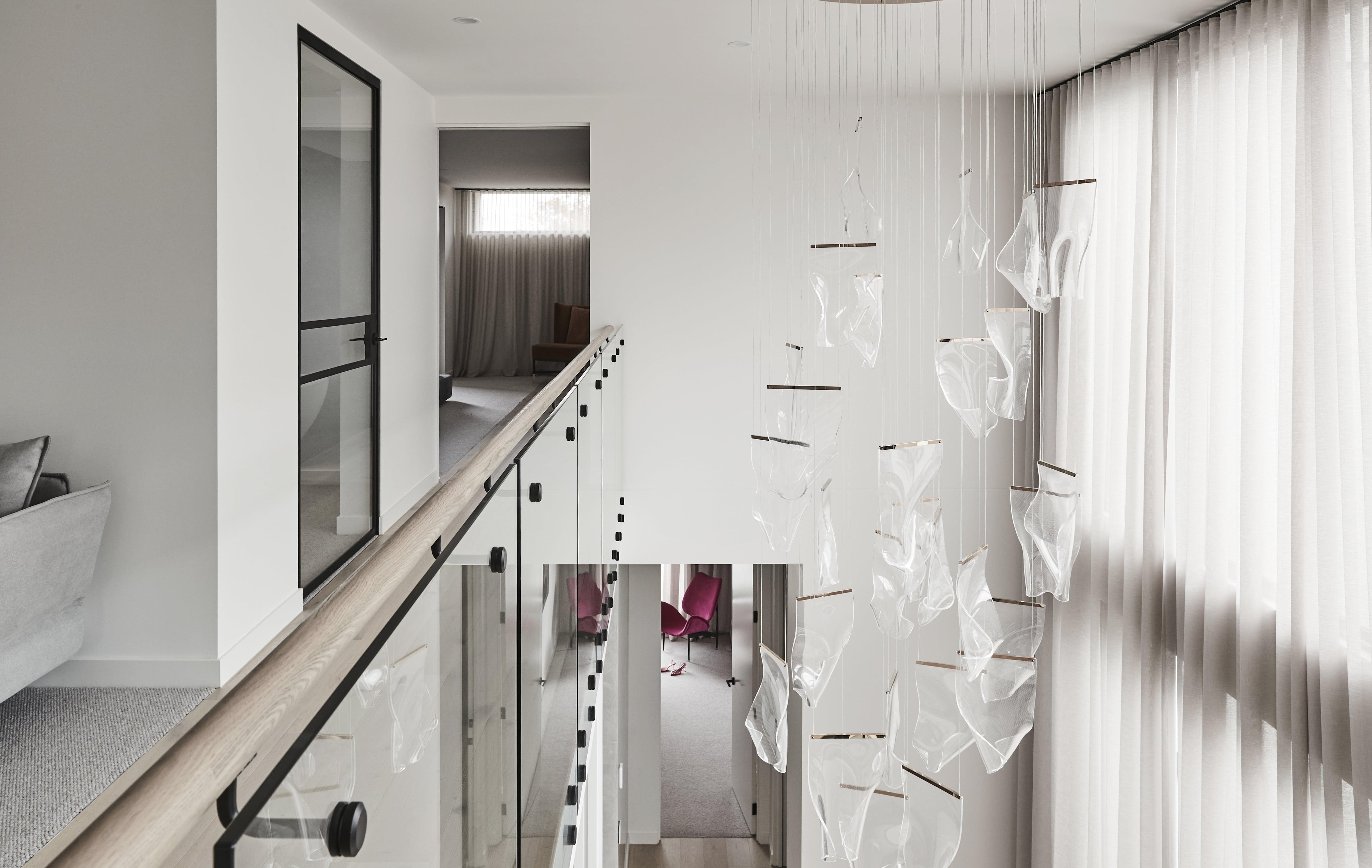 Thomas Archer Architecturally Designed void with a glass balcony, cascading transparent pendant lights, and large windows with sheer curtains. 