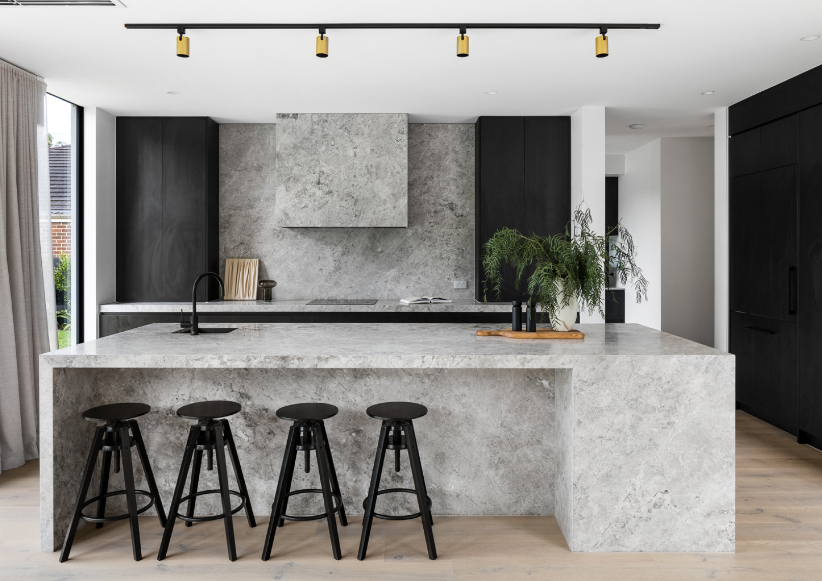 A contemporary kitchen featuring natural stone countertops, splashback and rangehood