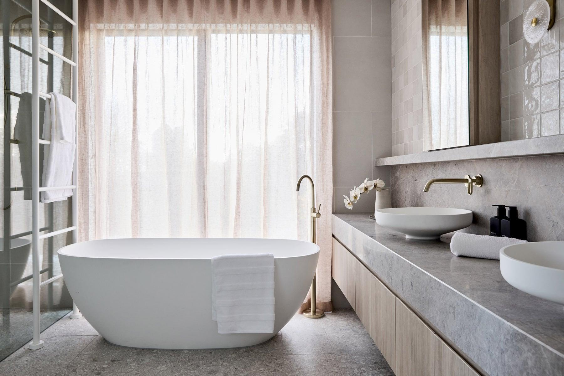 Thomas Archer Designed Elba Display Master Ensuite with large freestanding tub, stone benches and large windows with dusty pink sheer curtains