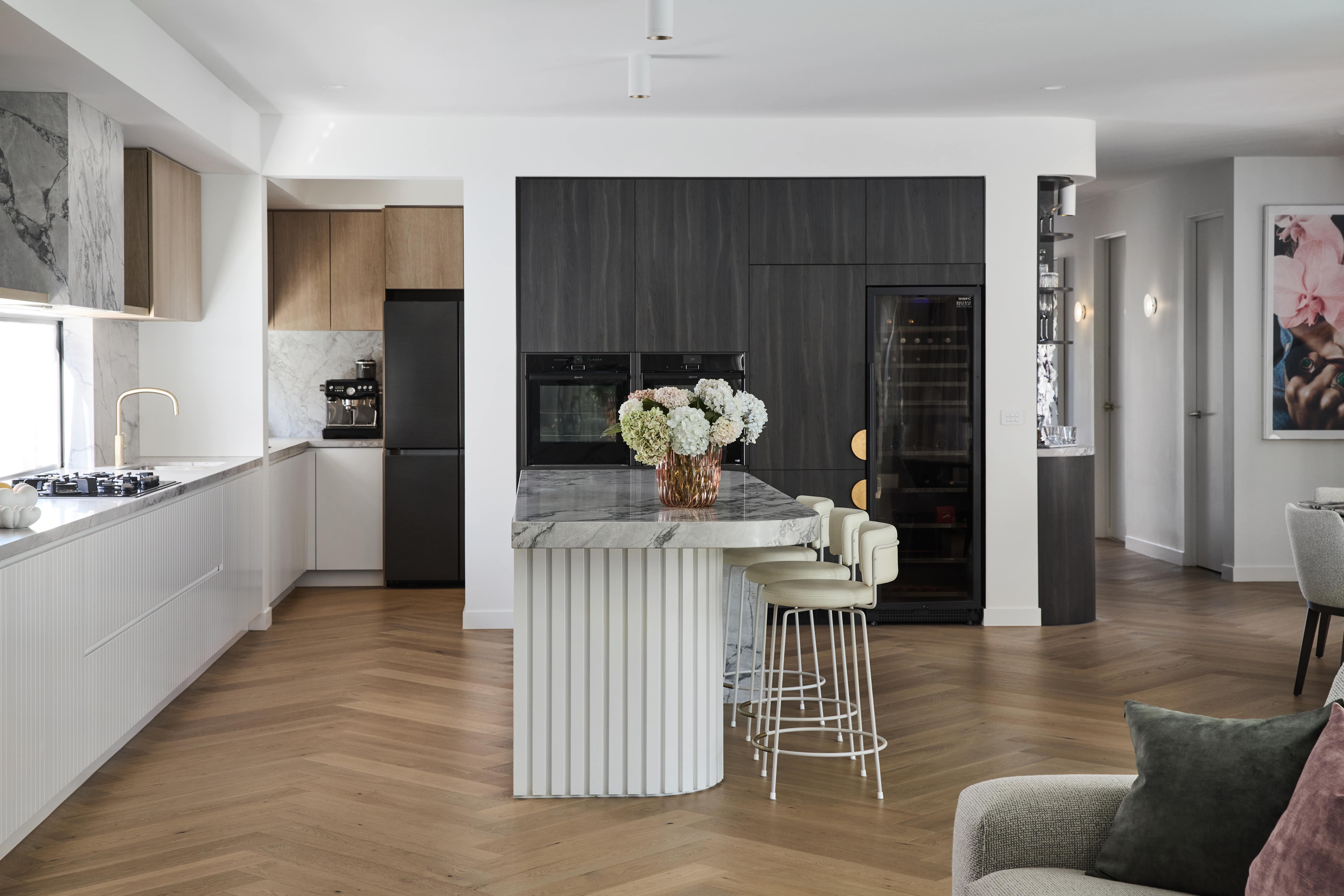 Open-plan contemporary kitchen featuring luxurious finishes, statement herringbone flooring, and contrasting joinery, designed and built by Thomas Archer.