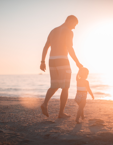 man and child walking along beach at sunset