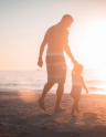 man and child walking along beach at sunset
