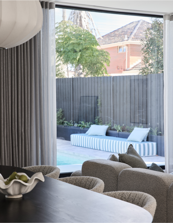 A spacious living room built by Thomas Archer featuring a large window overlooking a pool, filled with natural light and modern furnishings.