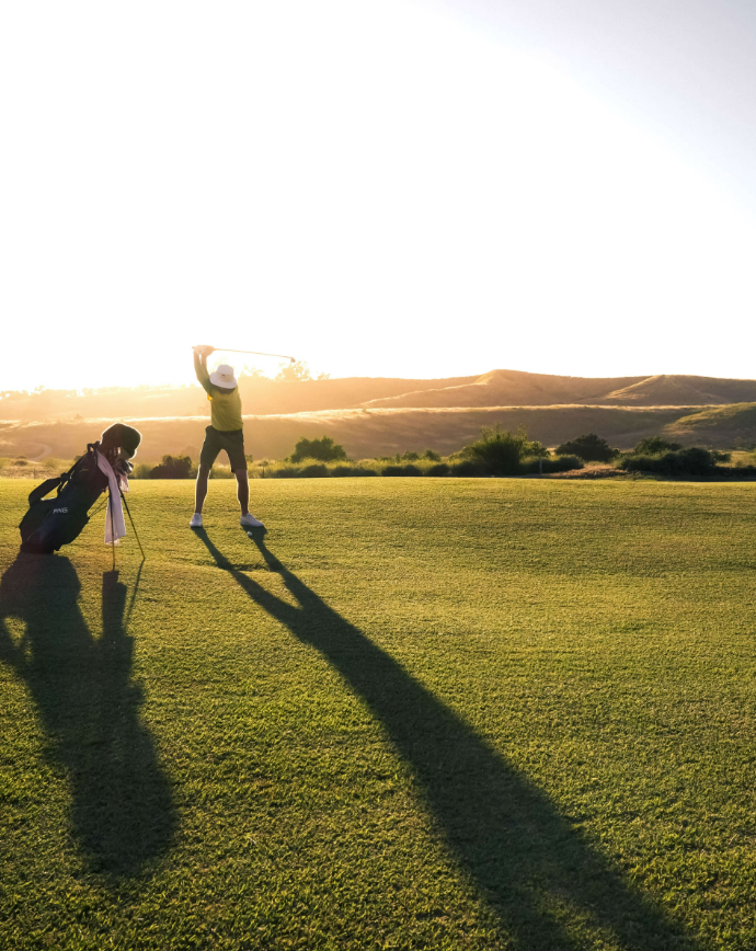 A golfer playing on a picturesque course as the sun sets in the background.
