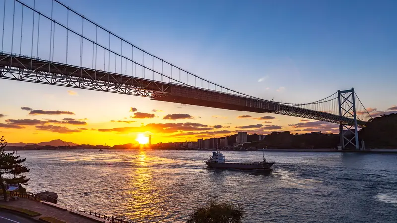 Kanmon Bridge over the Kanmon Strait at sunset with a ship on the water
