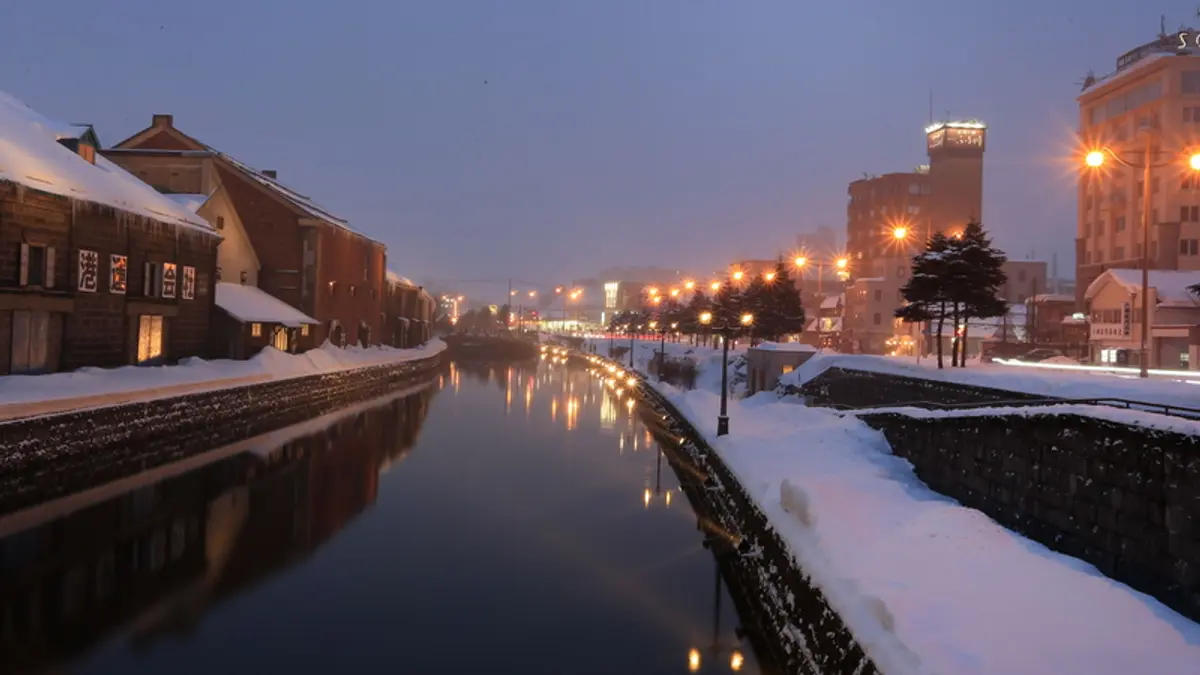 Snow-covered Otaru Canal and historic warehouses illuminated at dusk in Hokkaido, Japan