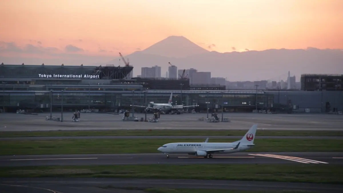 Mount Fuji behind Tokyo International Airport, with a JAL Express aircraft and white runway markings in the foreground