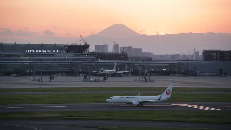 Mount Fuji behind Tokyo International Airport, with a JAL Express aircraft and white runway markings in the foreground