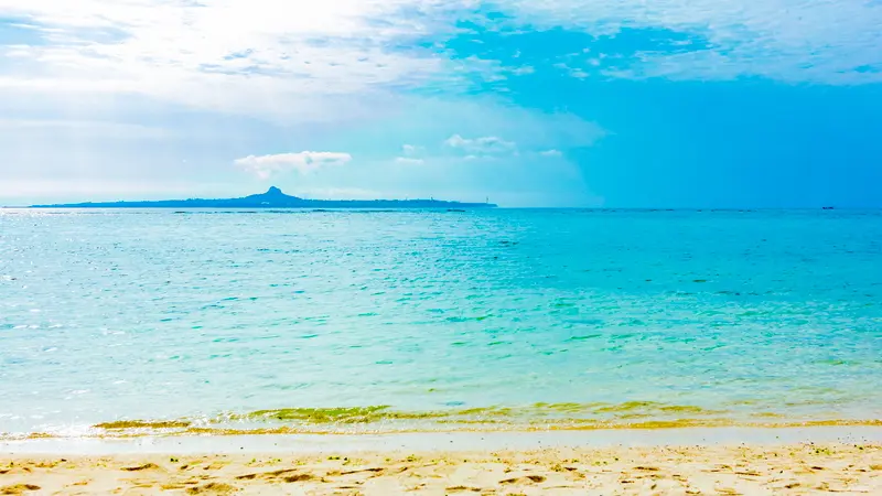 White sandy beach and emerald-green sea on Okinawa Main Island, with Ie Island on the horizon