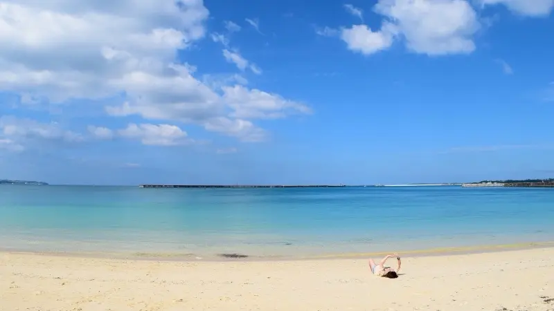 Person relaxing on a sandy beach in Okinawa beside turquoise sea under a blue sky