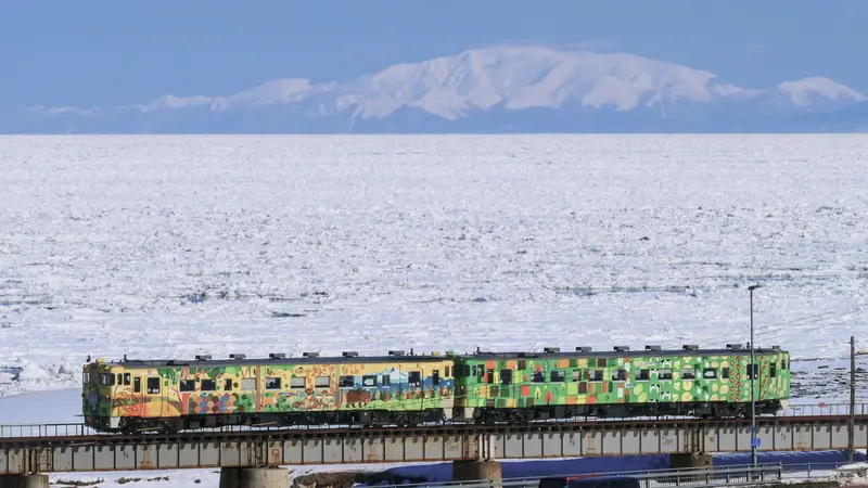 A Senmo Main Line train beside drift ice on the Sea of Okhotsk, with Mount Shiretoko in the background