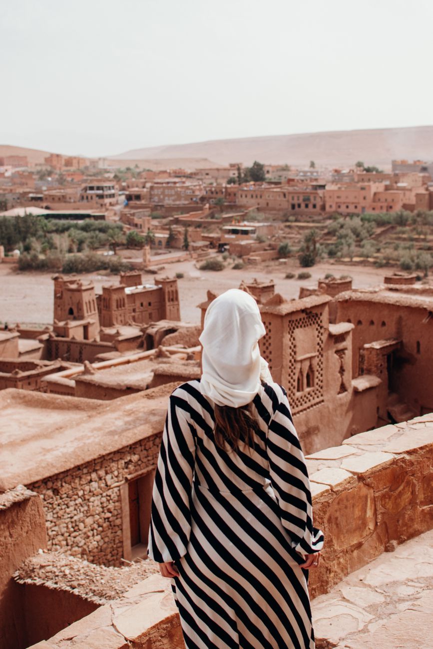 Woman in a striped dress and headscarf admiring Aït Benhaddou's desert architecture.