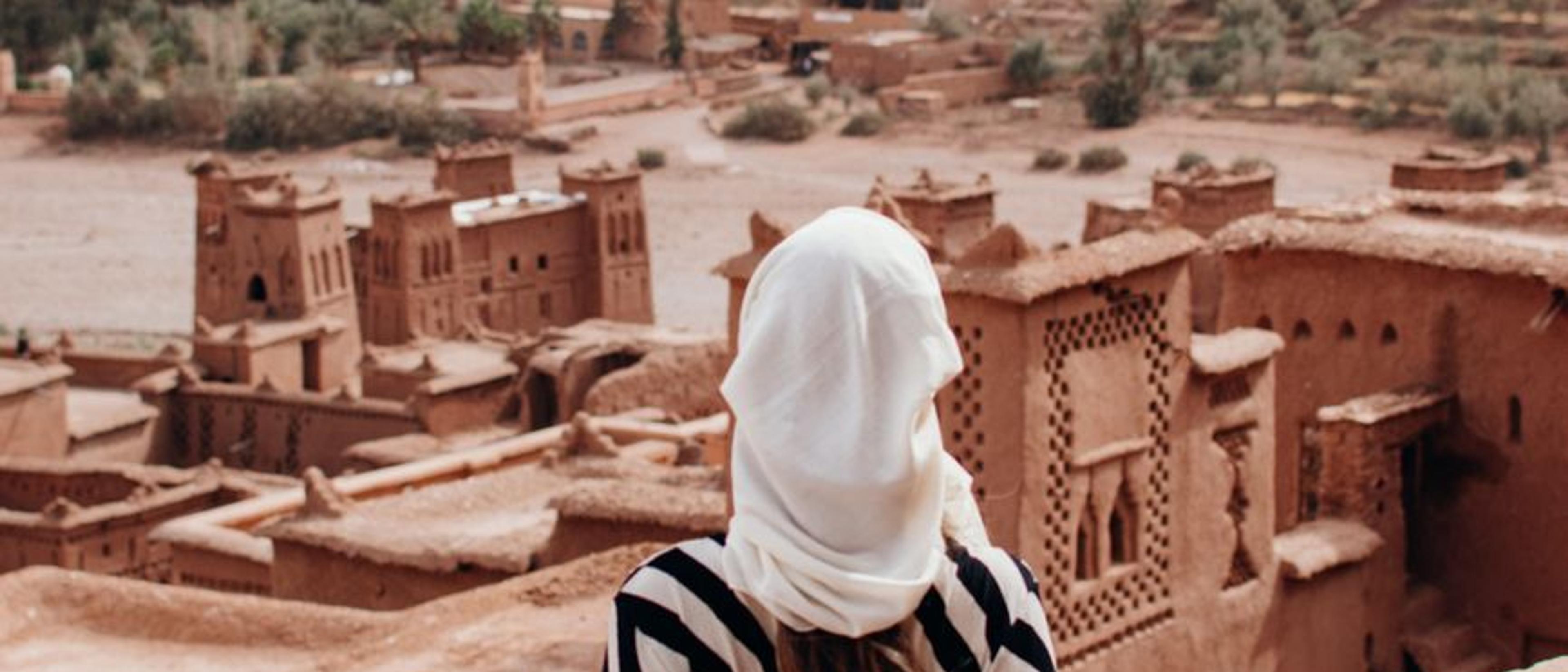 Woman in a striped dress and headscarf admiring Aït Benhaddou's desert architecture.