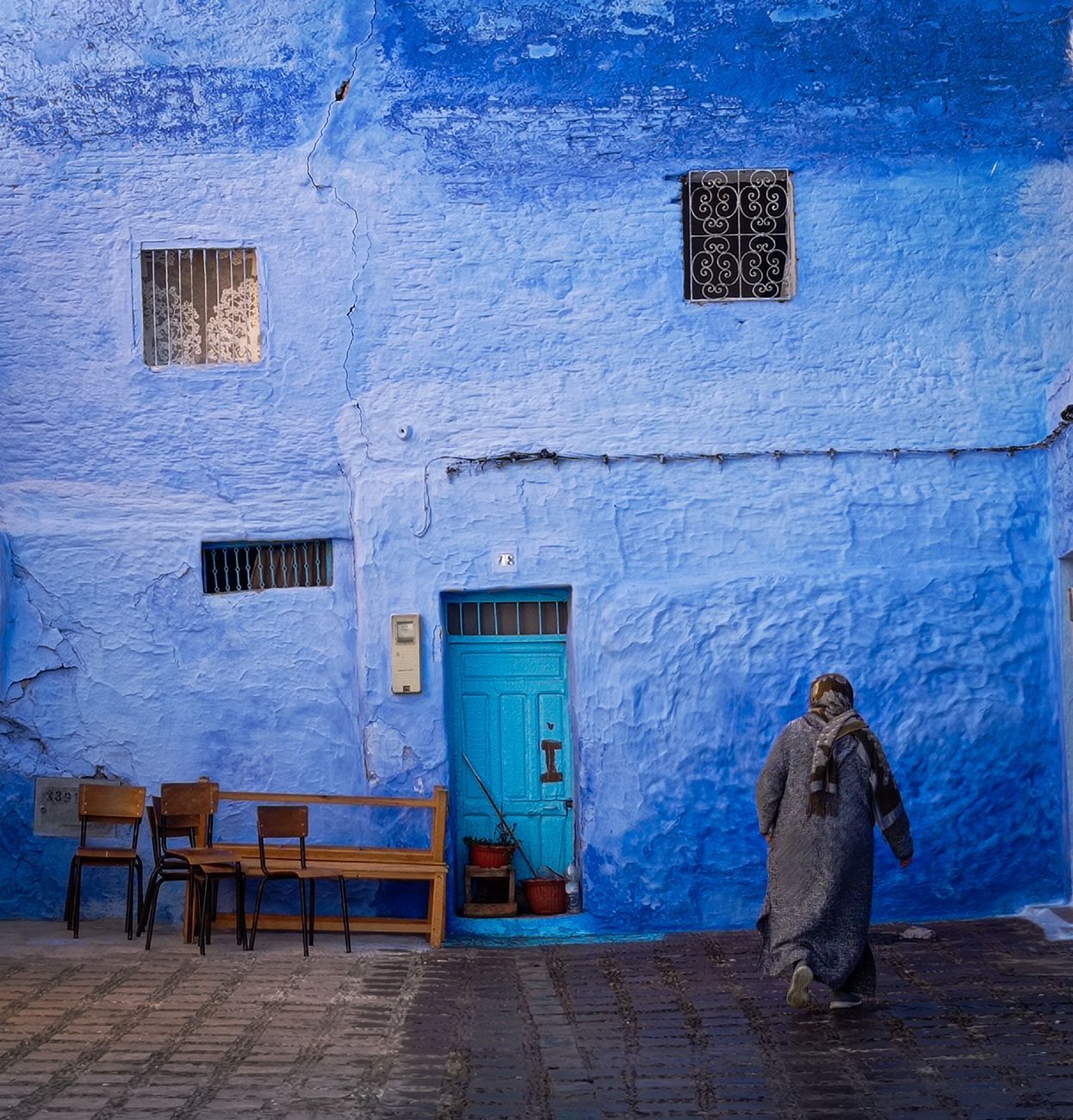 A person walks by a vibrant blue-painted wall in Chefchaouen, Morocco. Captivating street scene with vivid colors.